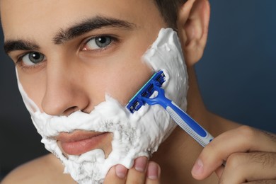 Photo of Handsome young man shaving with razor on blue background, closeup