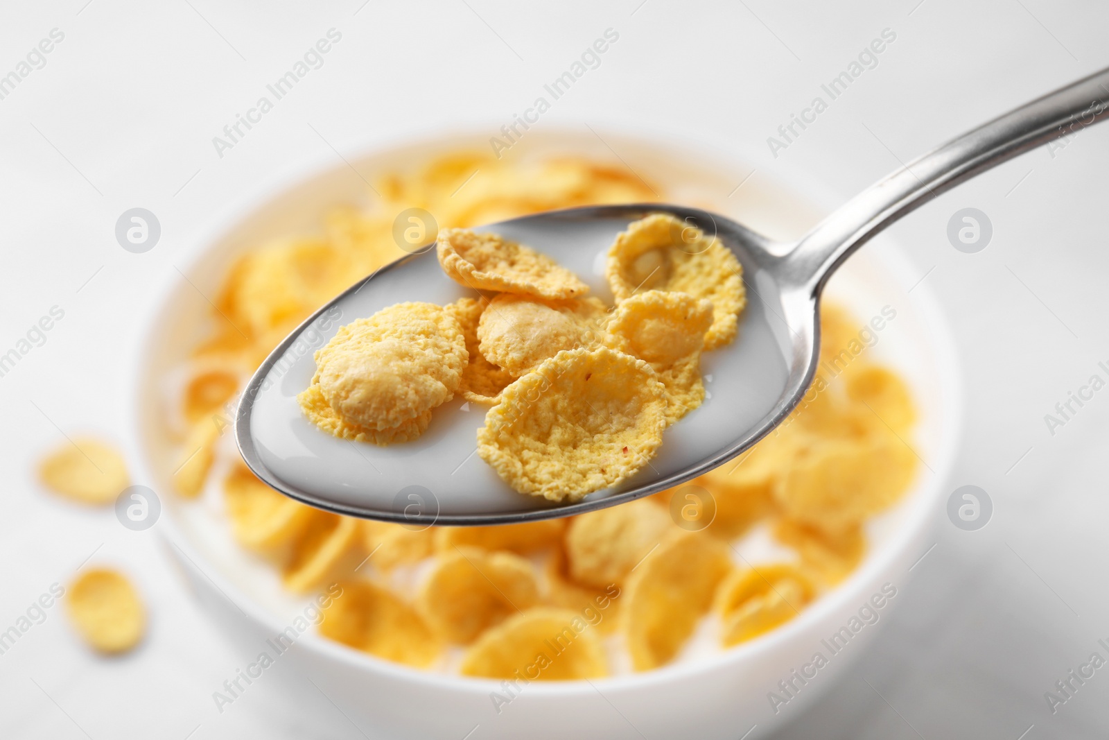 Photo of Breakfast cereal. Eating tasty corn flakes with milk at white table, closeup