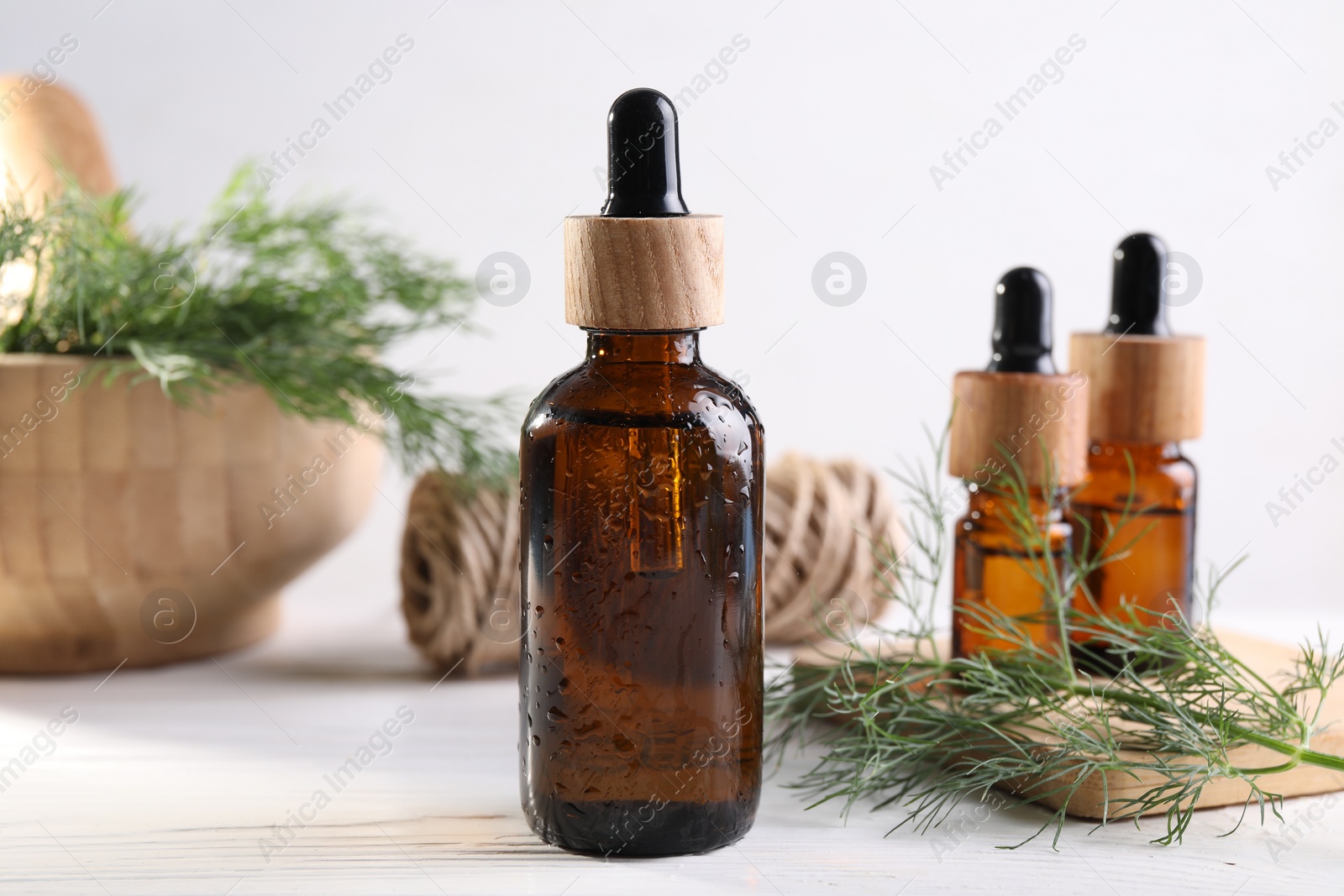 Photo of Bottles of essential oil and fresh dill on white table, closeup