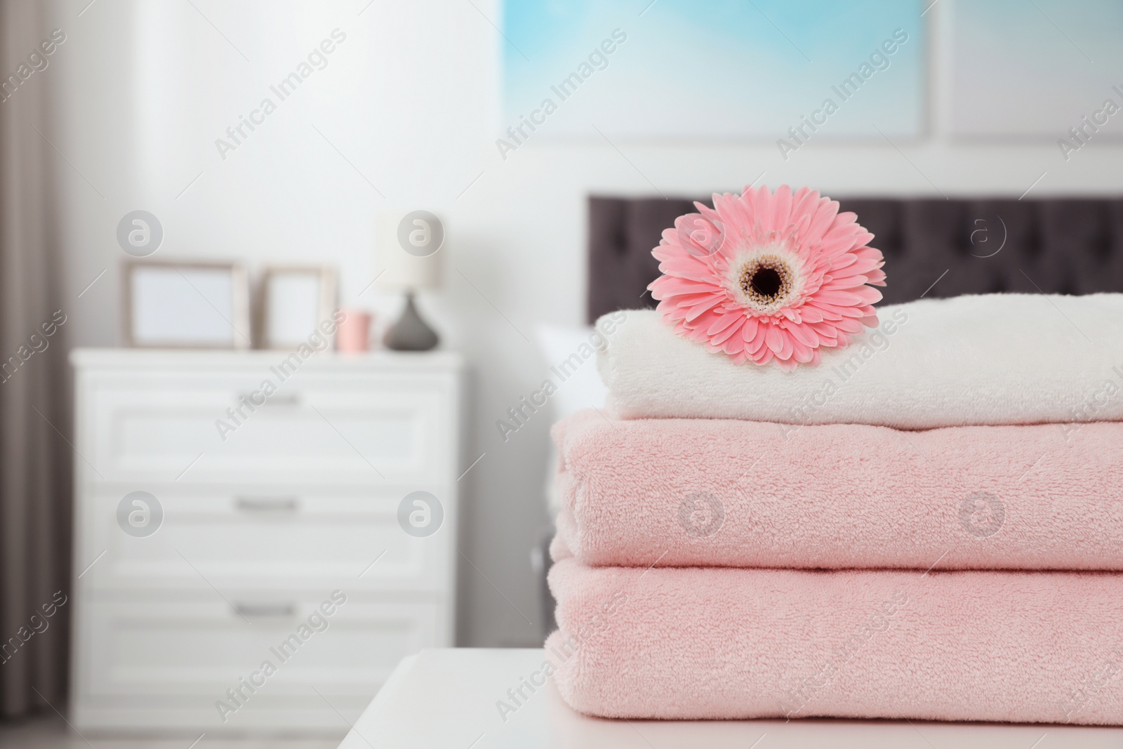 Photo of Stack of clean towels with flower on table in bedroom. Space for text