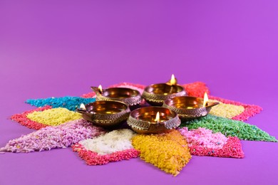 Diwali celebration. Diya lamps and colorful rangoli on purple background