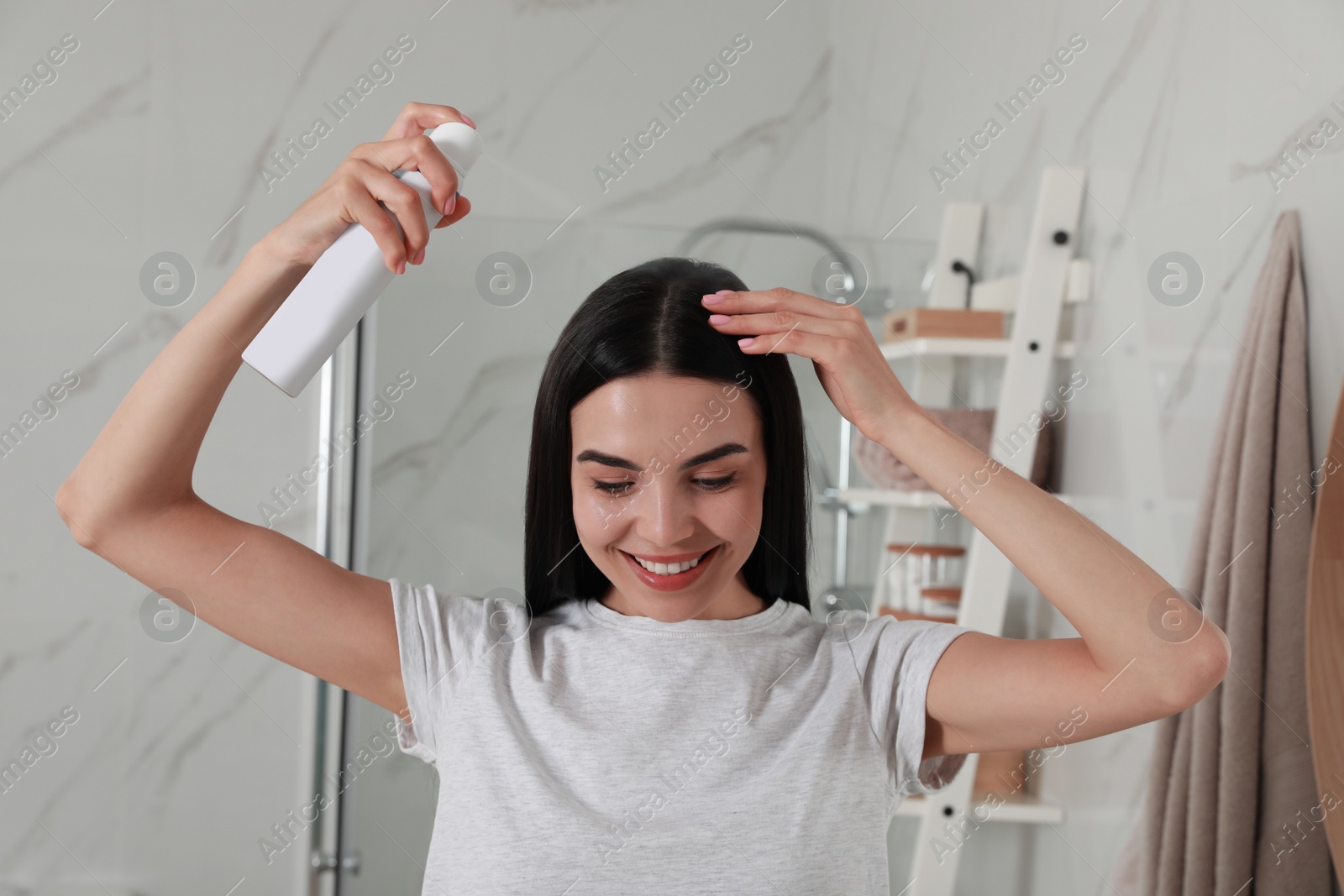 Photo of Woman applying dry shampoo onto her hair in bathroom