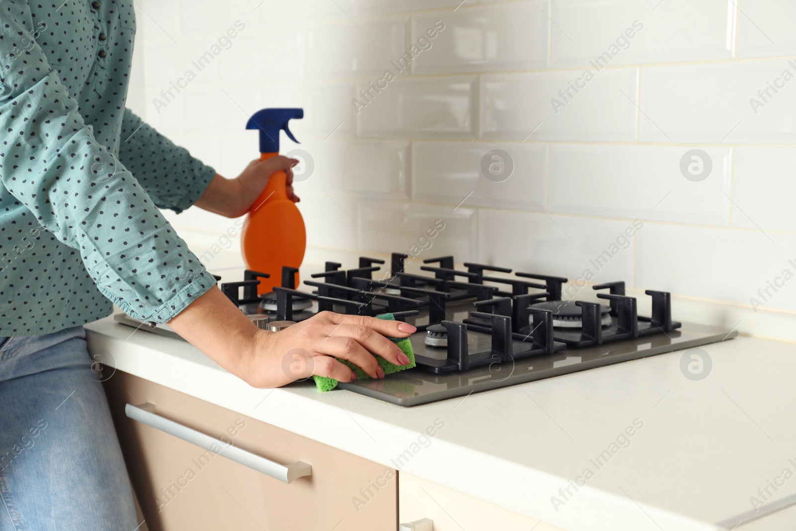 Photo of Woman cleaning gas stove with sponge in kitchen, closeup