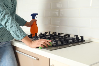 Photo of Woman cleaning gas stove with sponge in kitchen, closeup