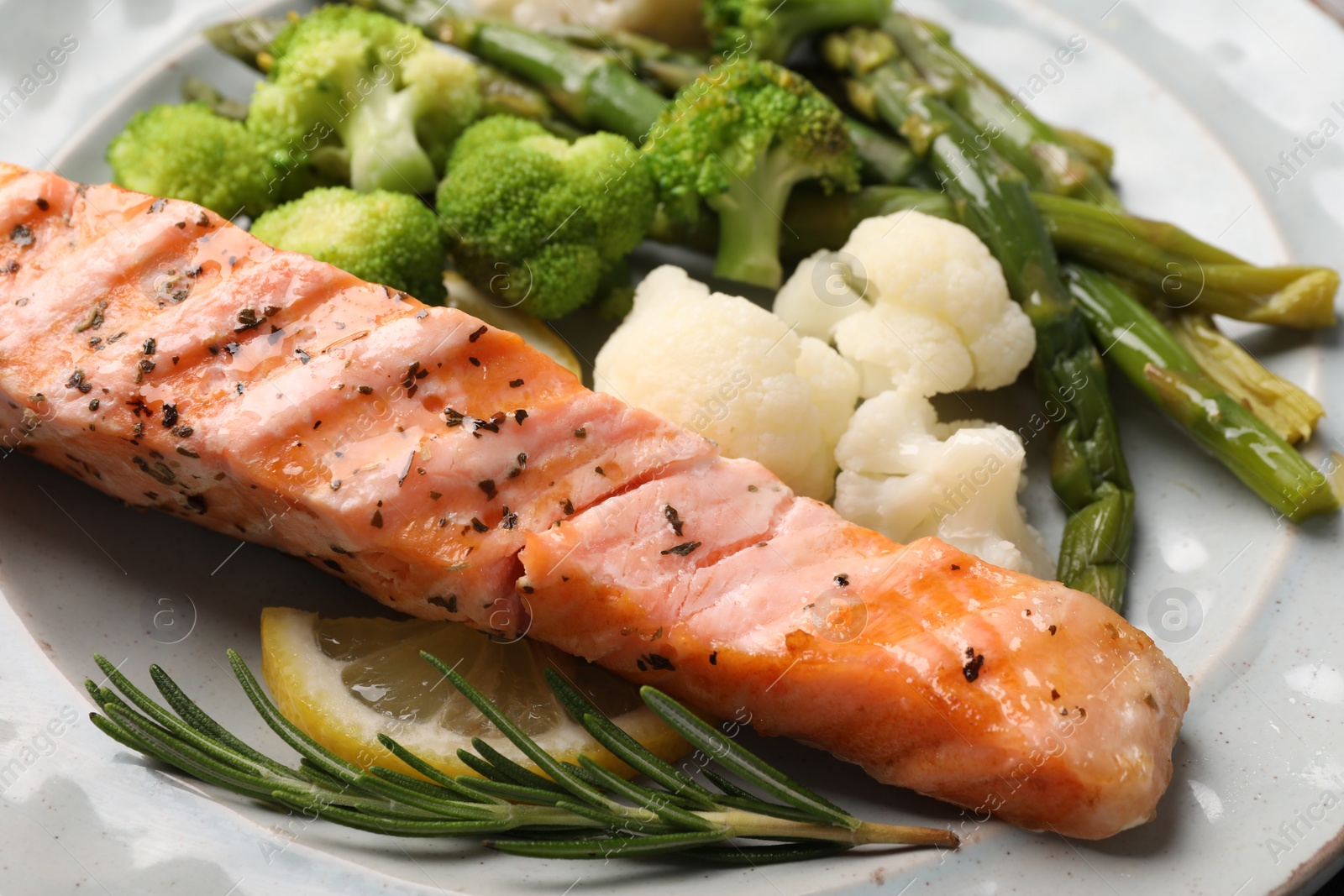 Photo of Healthy meal. Piece of grilled salmon, vegetables, asparagus, lemon and rosemary on plate, closeup