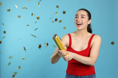 Young woman blowing up party popper on light blue background