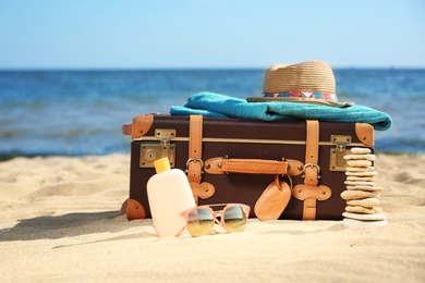 Suitcase and beach accessories on sand near sea