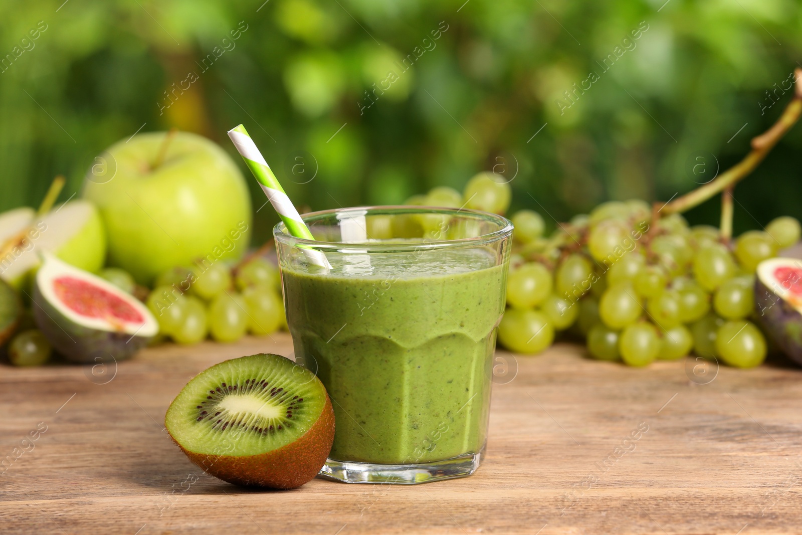 Photo of Glass of fresh green smoothie and ingredients on wooden table outdoors, space for text