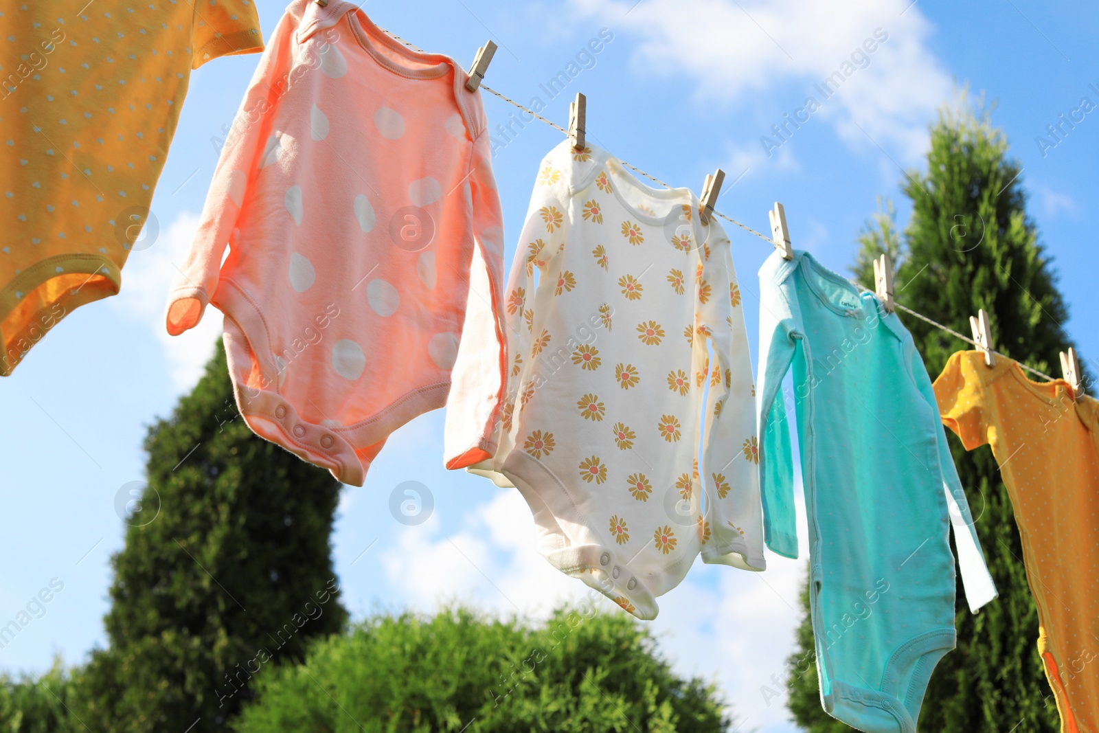 Photo of Clean baby onesies hanging on washing line outdoors. Drying clothes