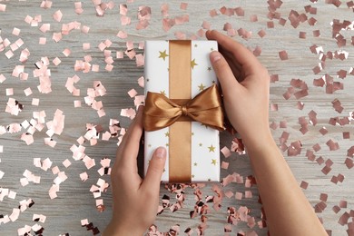 Photo of Christmas present. Woman with gift box and confetti at wooden table, top view