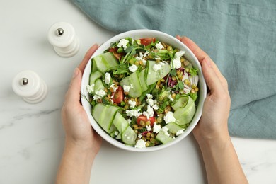 Photo of Woman holding bowl of delicious salad with lentils, vegetables and feta cheese at white table, top view