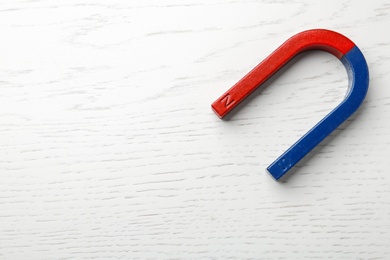 Photo of Red and blue horseshoe magnet on wooden background, top view with space for text