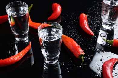 Photo of Red hot chili peppers and vodka on black table