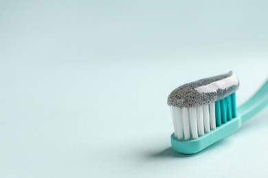 Brush with charcoal toothpaste on light background, closeup. Space for text