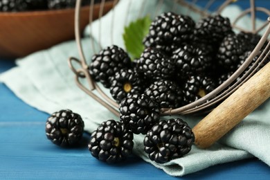 Photo of Basket with scattered fresh ripe blackberries on blue wooden table, closeup