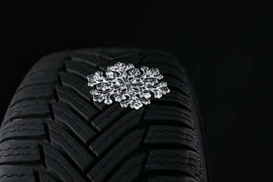 Photo of Winter tire with icy snowflake on black background, closeup