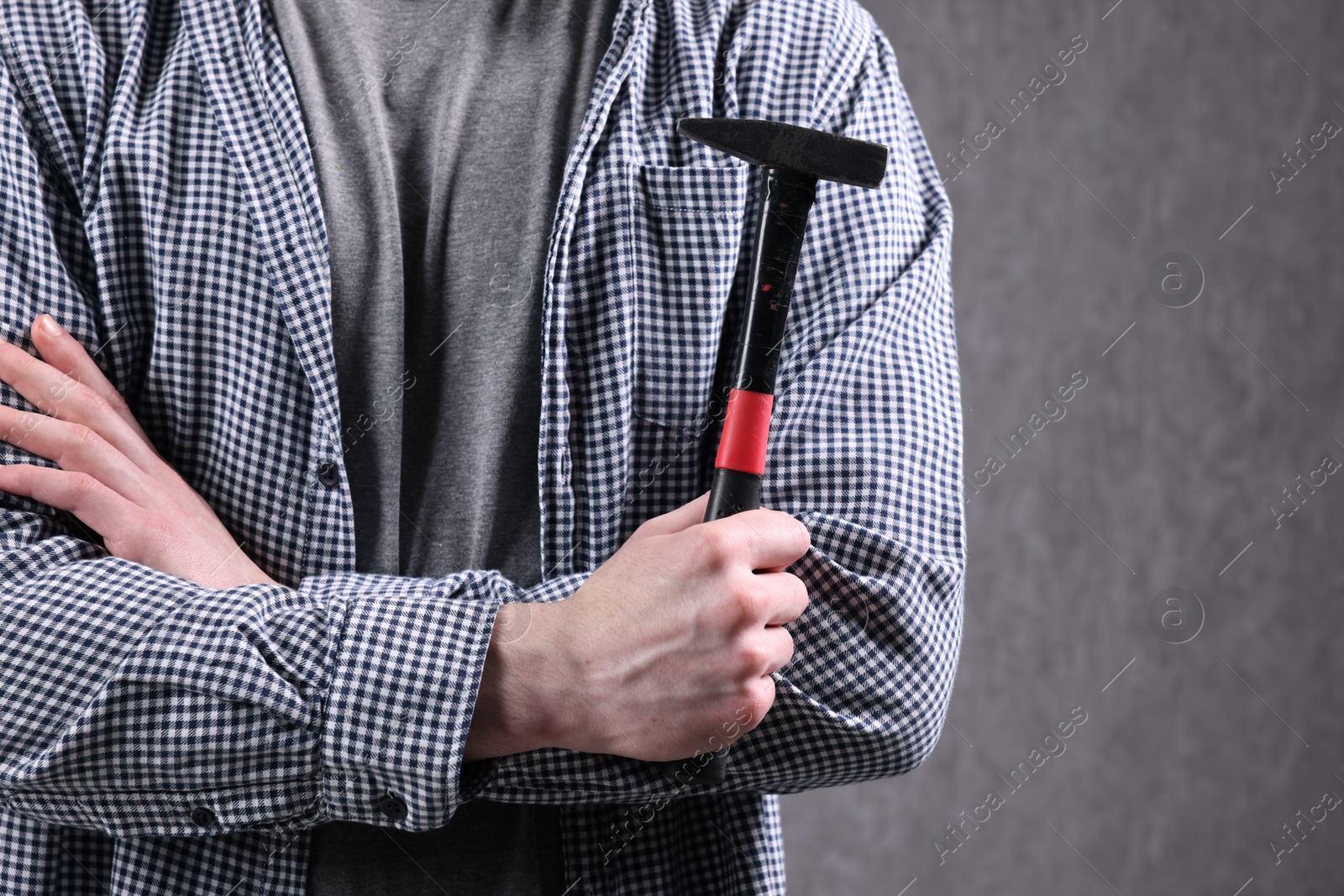 Photo of Young man holding hammer on grey background, closeup