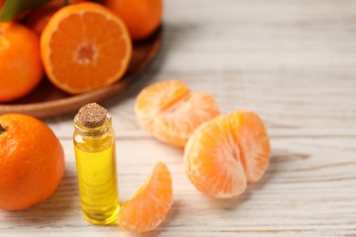 Photo of Bottle of tangerine essential oil and fresh fruits on white wooden table
