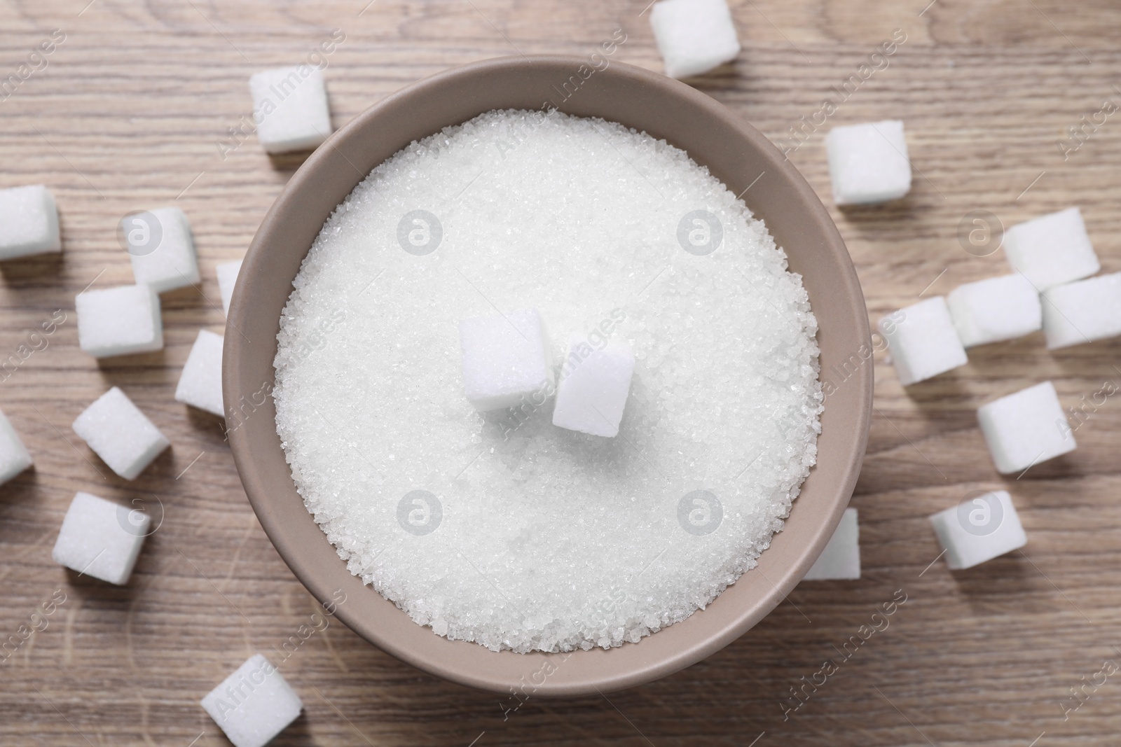 Photo of Different types of white sugar in bowl on wooden table, top view