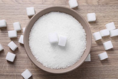 Different types of white sugar in bowl on wooden table, top view