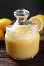 Photo of Delicious lemon curd in glass jar and fresh citrus fruits on wooden table