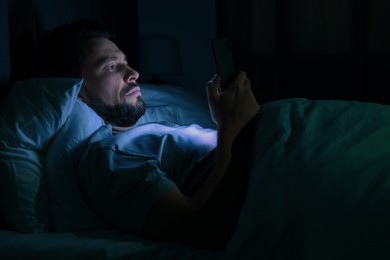 Photo of Man using smartphone in bed at night. Internet addiction