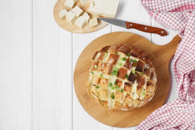 Photo of Freshly baked bread with tofu cheese, green onions and knife on white wooden table, flat lay. Space for text