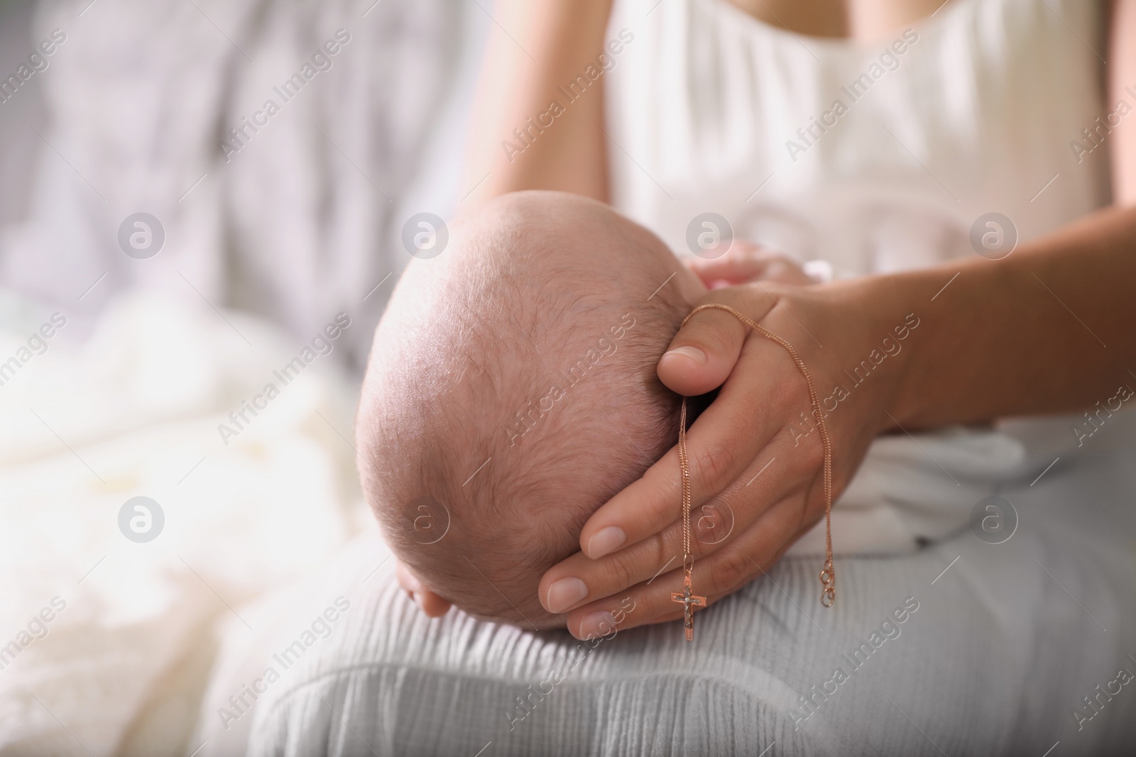 Photo of Mother holding newborn baby and Christian cross indoors, focus on hand