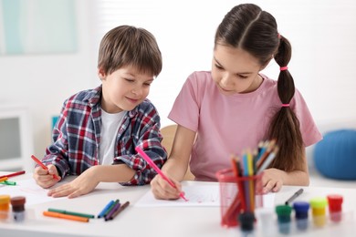 Photo of Happy brother and sister drawing at white table in room