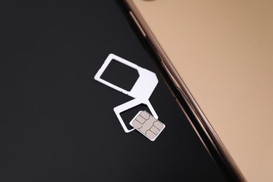 Photo of SIM card and smartphone on black background, above view
