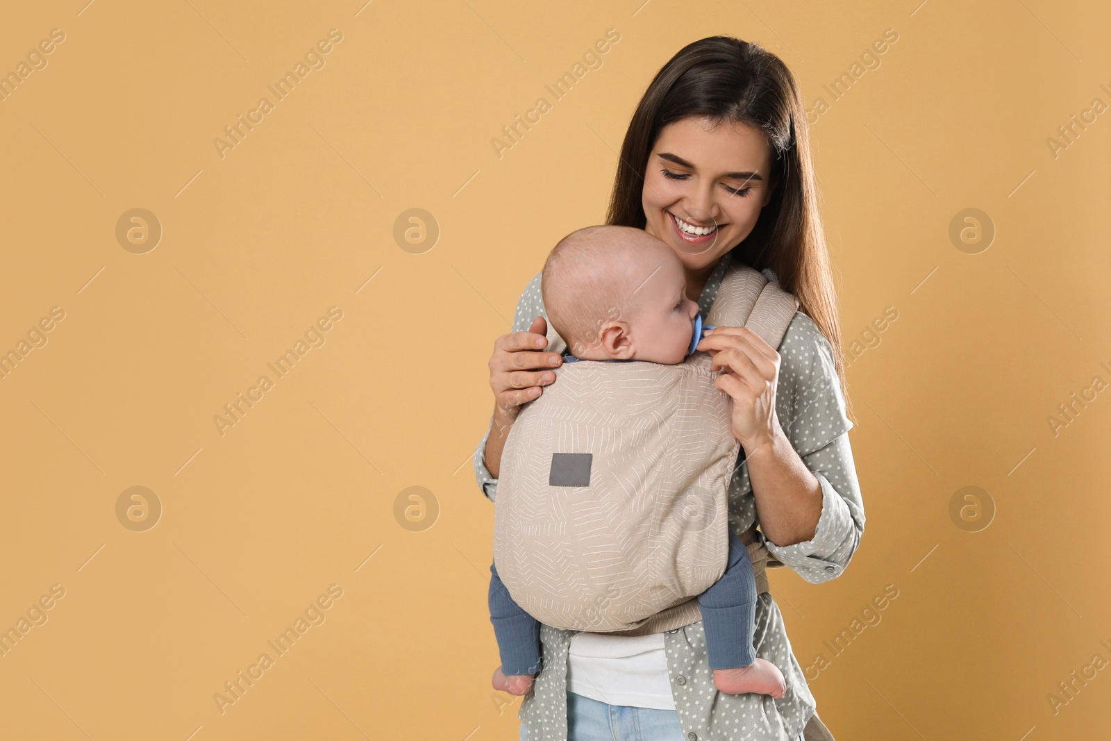 Photo of Mother holding her child in sling (baby carrier) on beige background. Space for text