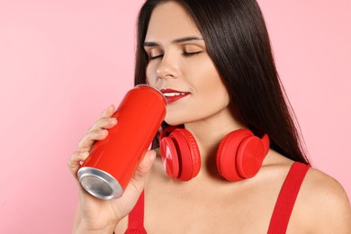 Photo of Beautiful young woman with headphones drinking from tin can on pink background, closeup