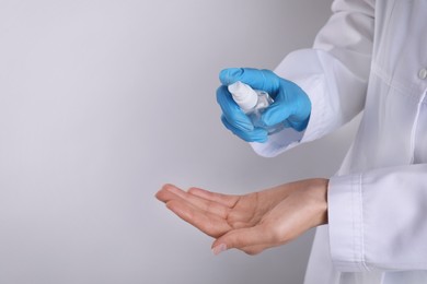 Doctor spraying antiseptic onto palm on light grey background, closeup. Space for text