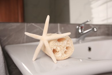 Photo of Natural loofah sponge and starfish on washbasin in bathroom