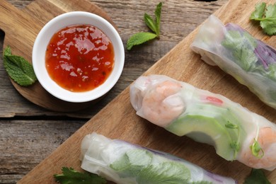 Delicious spring rolls and sauce on wooden table, top view