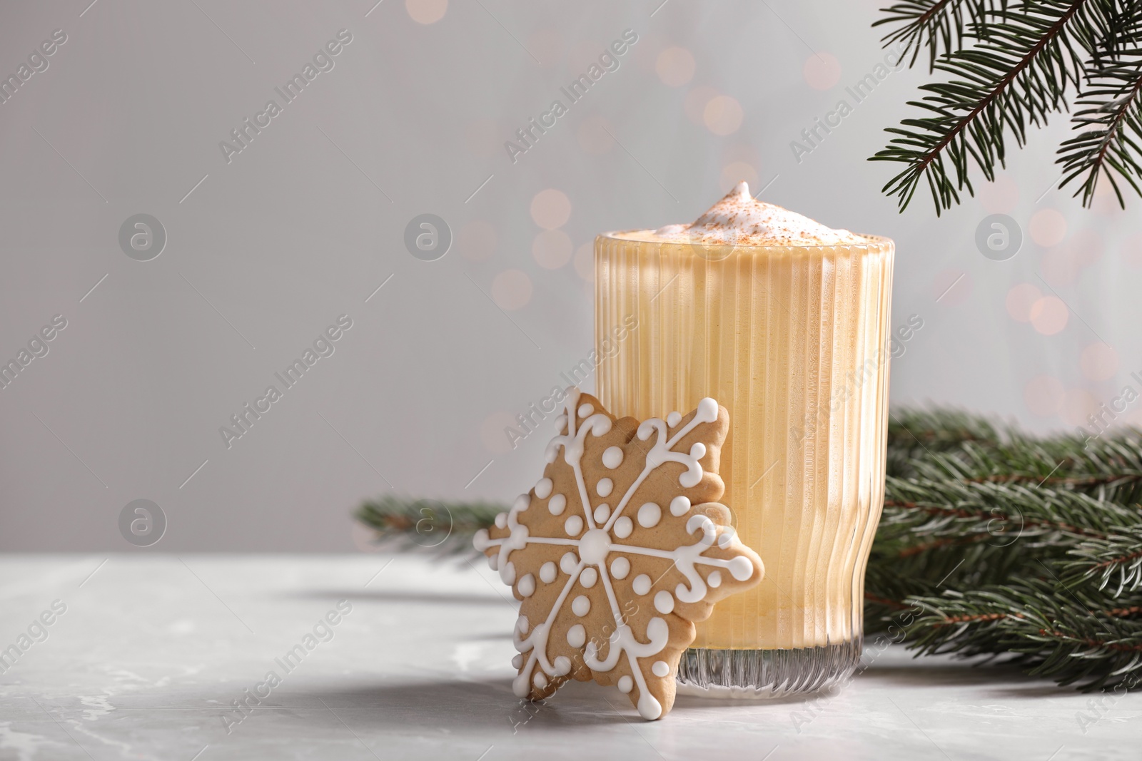 Photo of Tasty eggnog, cookie and fir branches on grey textured table, space for text