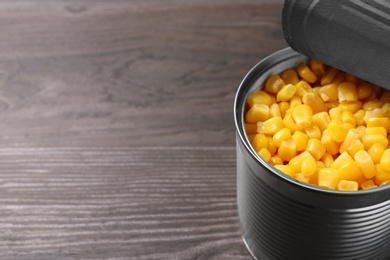 Open tin can of sweet corn on wooden table, closeup. Space for text