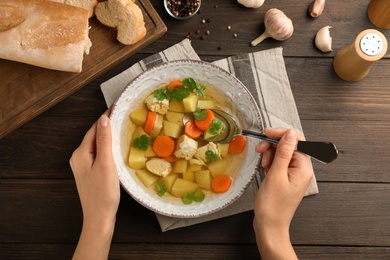 Photo of Young woman eating homemade chicken soup at table, top view