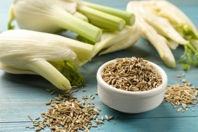 Photo of Fennel seeds in bowl and fresh vegetables on light blue wooden table, closeup