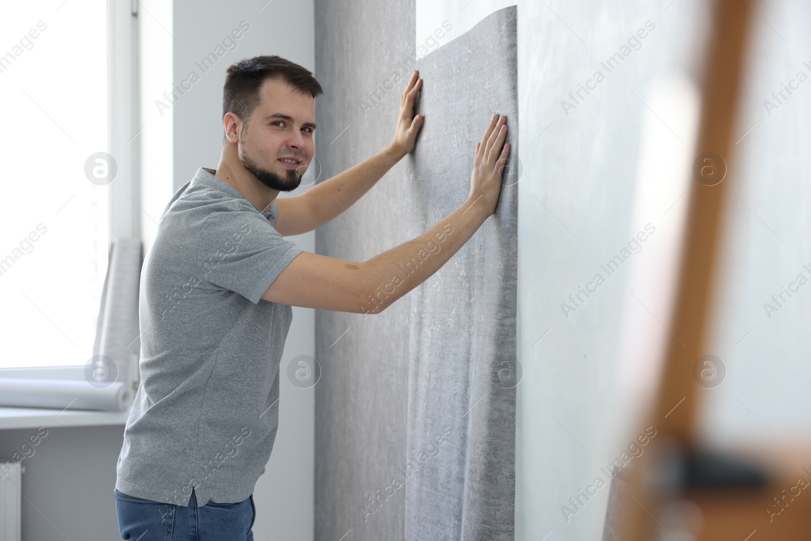 Photo of Man hanging stylish gray wallpaper in room