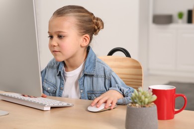 Photo of Little girl using computer at table in room. Internet addiction