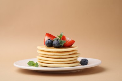 Photo of Delicious pancakes with strawberries, blueberries and mint on dark beige background