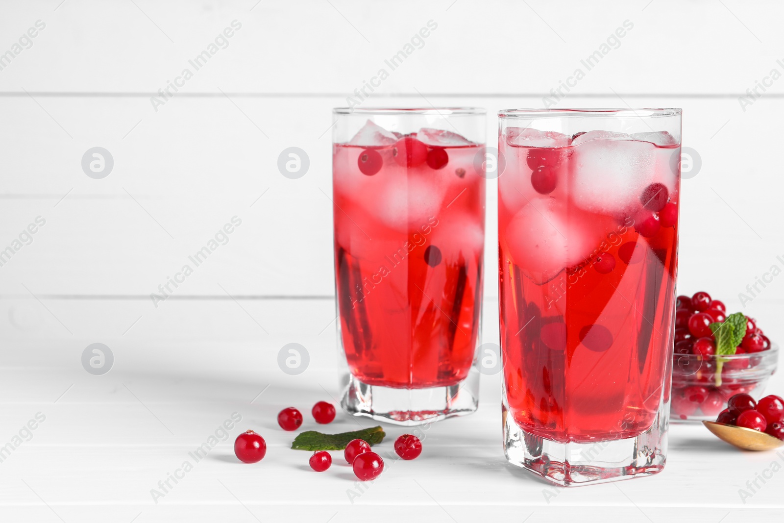 Photo of Tasty cranberry juice with ice cubes in glasses and fresh berries on white wooden table. Space for text