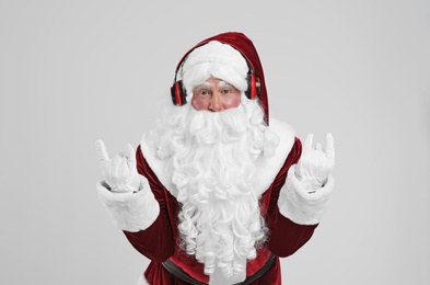 Photo of Santa Claus with headphones listening to Christmas music on light grey background