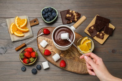 Photo of Woman dipping sweet marshmallow in fondue pot with melted chocolate at wooden table, top view