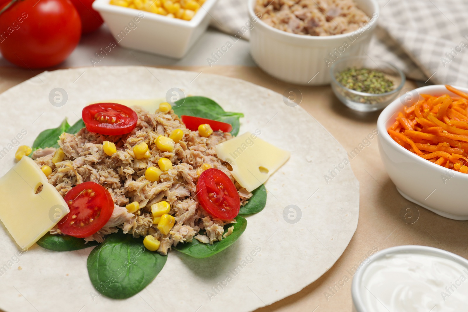 Photo of Delicious tortilla with tuna, vegetables and cheese on light table, closeup. Cooking shawarma