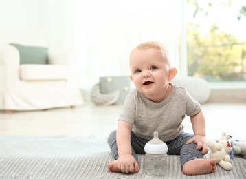 Cute baby with bottle sitting on floor in room. Space for text