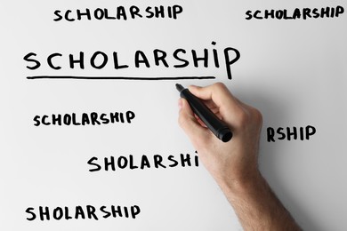 Man writing word SCHOLARSHIP on whiteboard, closeup