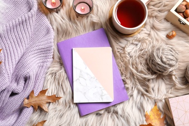 Photo of Flat lay composition with notebooks, cup of tea and warm clothes on fuzzy rug