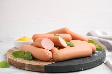 Photo of Delicious boiled sausages and basil on light table against white background, closeup